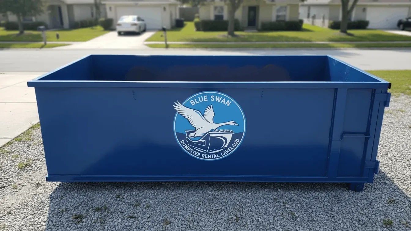 Roll-off dumpster rental in Lakeland: a 20 yard container being winched off the truck bed onto doubled plywood on a residential concrete drive off Lakeland Highlands Road, with the driver watching the oak canopy and the overhead service drop. Roll-off dumpster rental in Lakeland: a 20 yard container being winched off the truck bed onto doubled plywood on a residential concrete drive off Lakeland Highlands Road, with the driver watching the oak canopy and the overhead service drop.