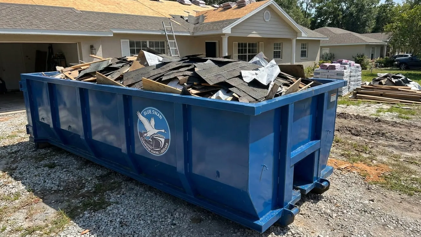Roofing dumpster rental in Lakeland: a 15 yard roll-off set tight beside the eave of a Cleveland Heights ranch on doubled plywood, half filled with three-tab shingle, felt and flashing loaded flat and a tarp folded over the rail against an afternoon storm. Roofing dumpster rental in Lakeland: a 15 yard roll-off set tight beside the eave of a Cleveland Heights ranch on doubled plywood, half filled with three-tab shingle, felt and flashing loaded flat and a tarp folded over the rail against an afternoon storm.